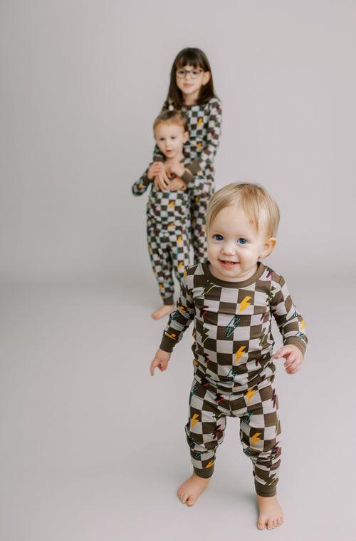 Three children wearing checkered pajamas standing on a plain background